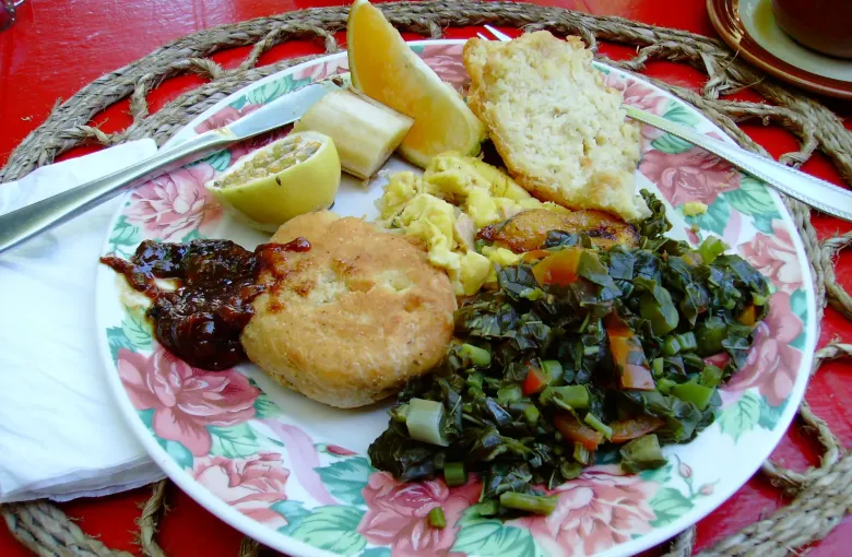 A breakfast plate of ackee and saltfish with callaloo, fried dumpling, banana and a wedge of lime.