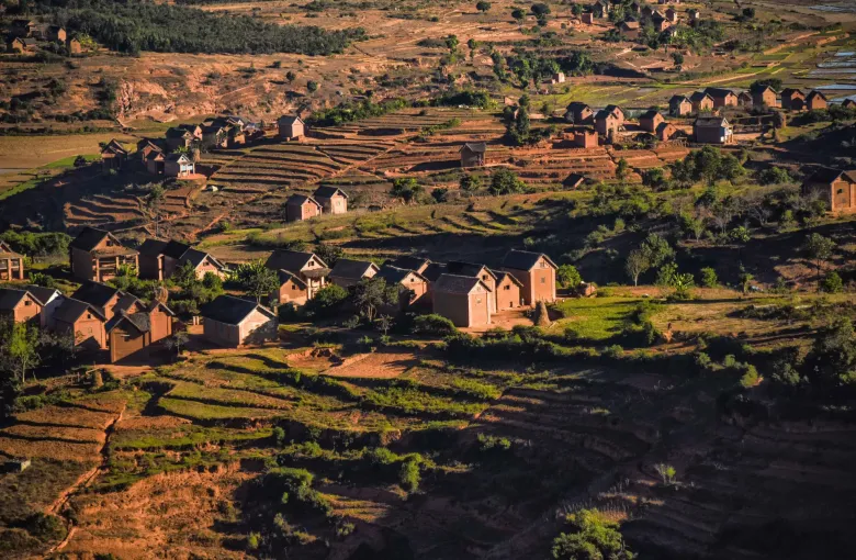 Low sunlight across a terraced valley and a cluster of village houses in the Malagasy highlands.