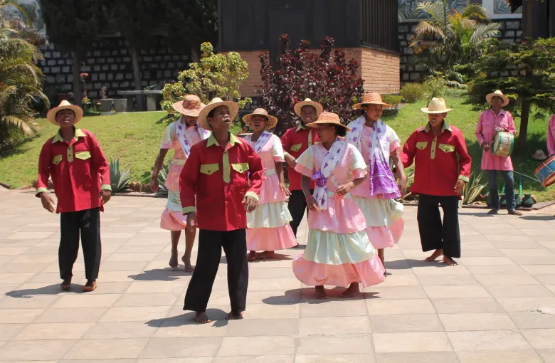 A hiragasy troupe in red jackets and pink dresses performing on a paved square at Ambositra in the central highlands.