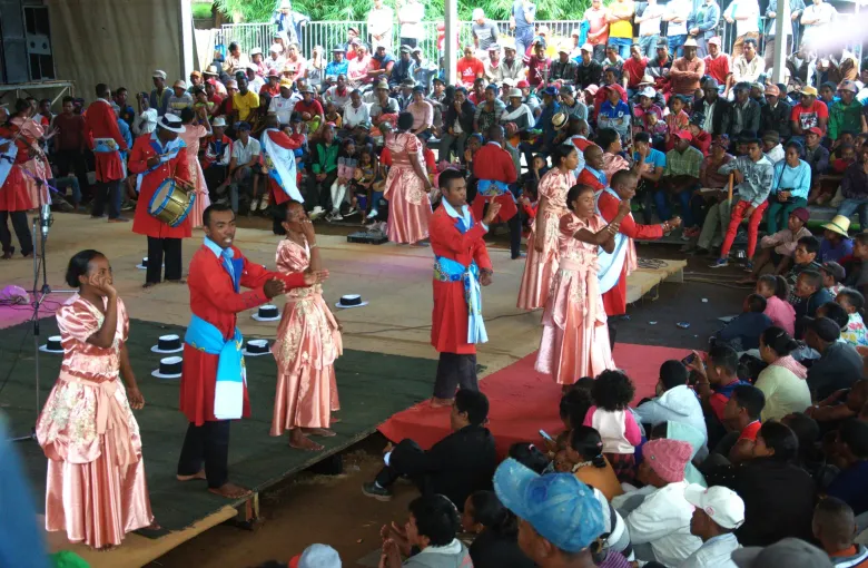 A hiragasy troupe performing in front of a seated crowd, the singers in wide pink dresses and the orators in red.