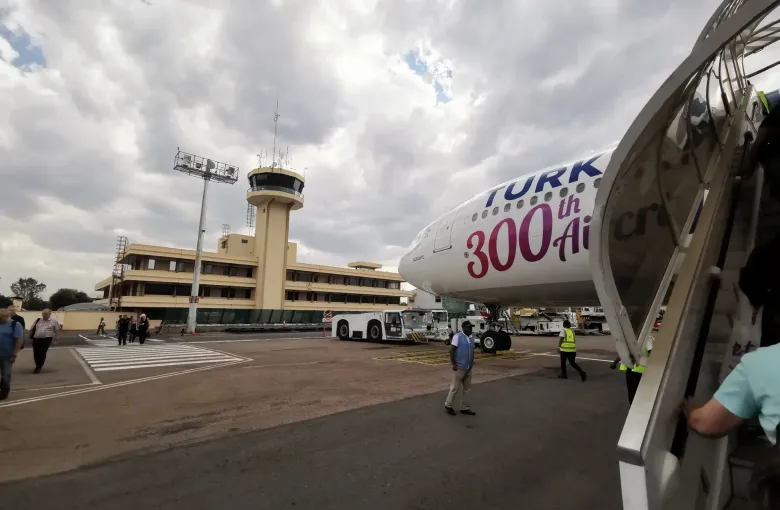 An airliner on the apron beside the terminal and control tower at Ivato International Airport, Antananarivo, under a heavy sky.