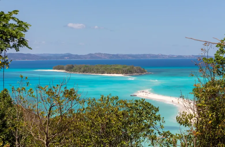 The pale sandbar joining the two islets of Nosy Iranja, seen from a wooded rise above turquoise shallow water in northwest Madagascar.