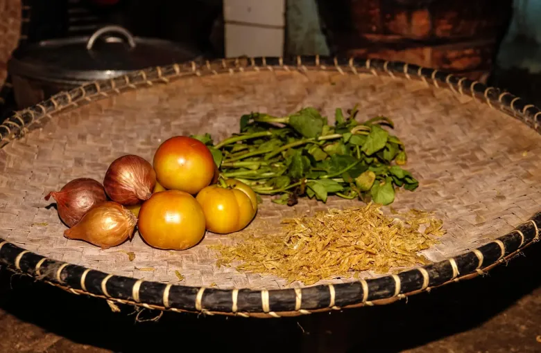 Onions, tomatoes, ginger and leafy brede greens arranged in a woven basket, the ingredients of romazava, the Malagasy national dish.