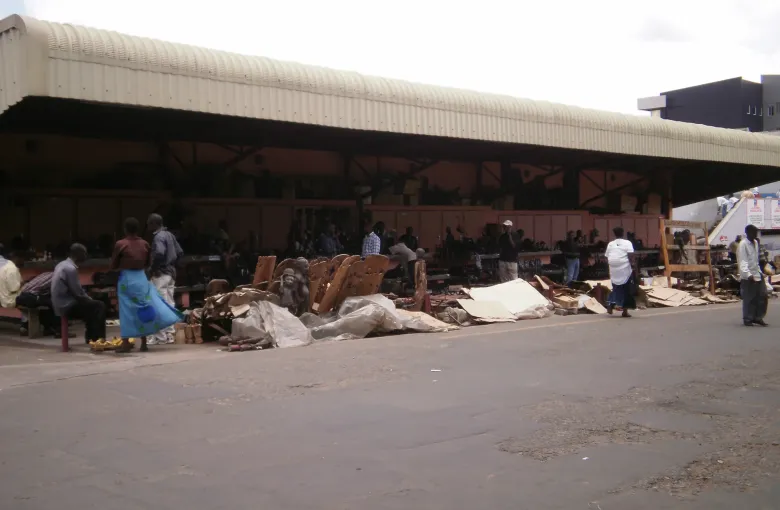 Traders and stalls under the long roof of a covered market in Blantyre, Malawi, with goods laid out on the ground.