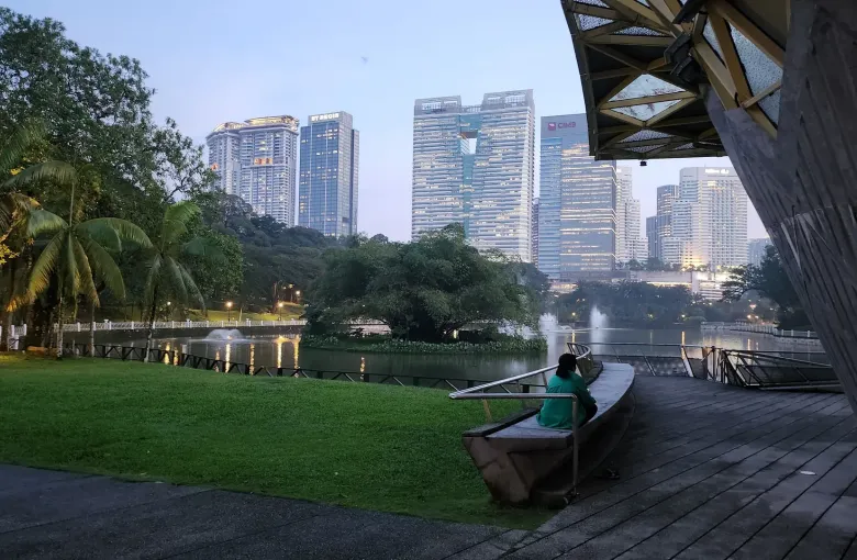 A lake and palms in the Perdana Botanical Gardens with the Kuala Lumpur skyline beyond.