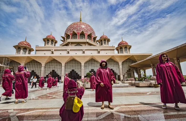 Visitors in the magenta robes lent to guests walk across the plaza in front of Putra Mosque, Putrajaya.