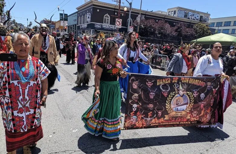 Members of a Oaxacan community from Juxtlahuaca parading in San Francisco behind a painted Danza de los Diablos banner.