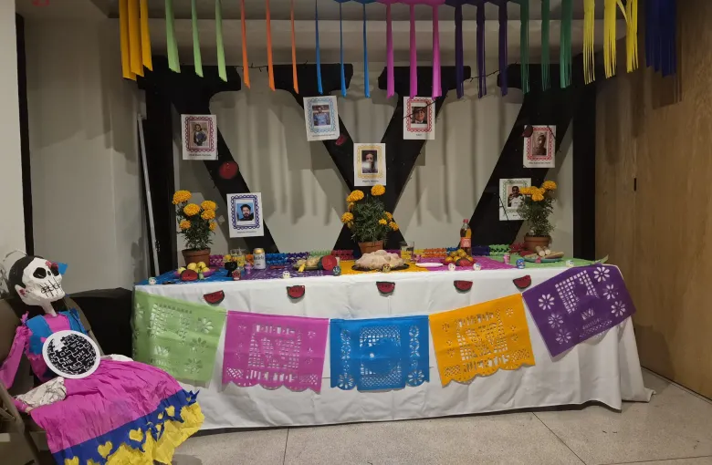 A Dia de Muertos ofrenda laid with photographs, marigolds and cut paper banners, with a catrina figure at one end.
