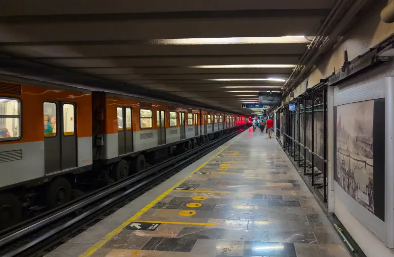 A level platform at Zocalo Tenochtitlan station on the Mexico City Metro with a train alongside and framed prints down the wall.