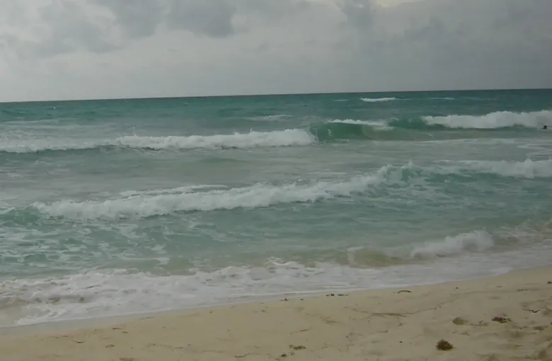 An open stretch of sand and shallow surf at Playa del Carmen on the Caribbean coast of Quintana Roo under a clouded sky.