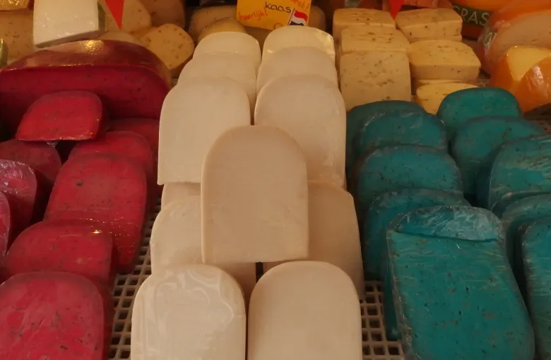 Wheels and blocks of Dutch cheese stacked on a market stall in red, green and plain yellow wax.