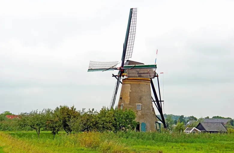 A brick drainage windmill standing above flat green polder, its sails bare against a low even gray sky.