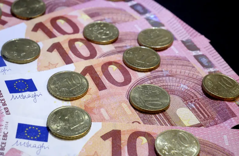 Ten euro banknotes fanned out with ten euro cent coins scattered across them.