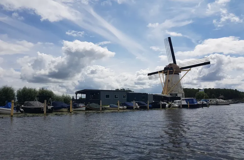 A drainage windmill at Kinderdijk beyond moored boats, with flat waterside paths running along the dyke in front of it.