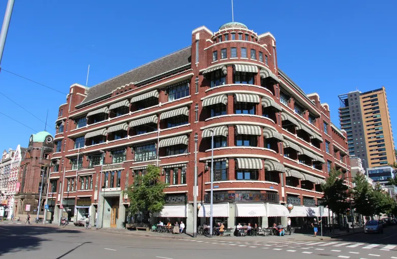 A curved brick office block with awnings and pavement cafes on a bright street corner in central Rotterdam.