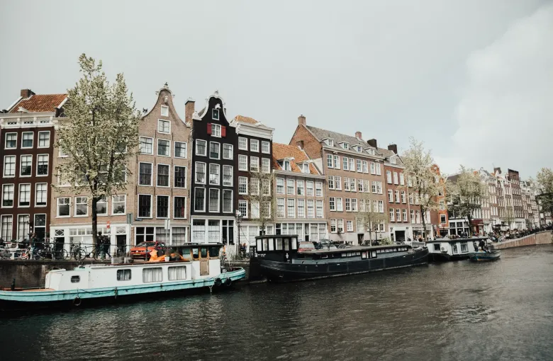 A row of narrow seventeenth-century canal houses with stepped and bell gables above moored barges on an Amsterdam canal.