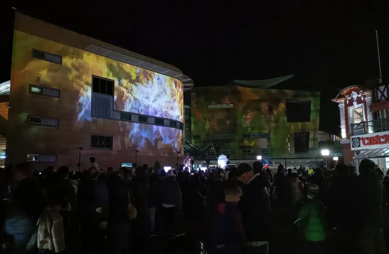 A crowd watching a light projection thrown across building facades during Matariki in Wellington.