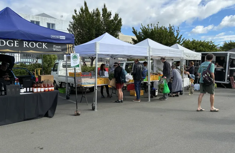 Stalls selling wine and produce under white canopies at the Otago Farmers Market in Dunedin.