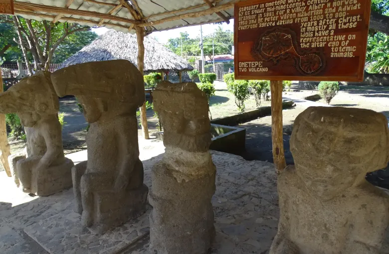Four carved basalt figures stand under a shelter at Altagracia on Ometepe Island, worn smooth by weather.