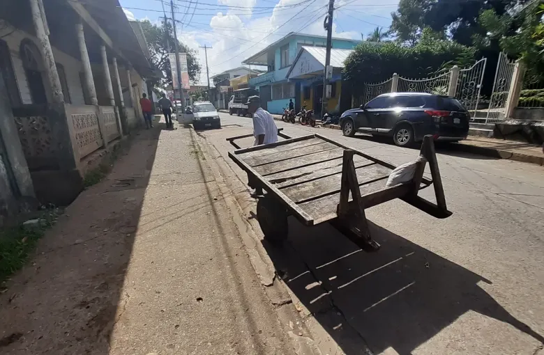 A man pushes a wooden handcart past fretworked timber houses on a quiet street in Bluefields.