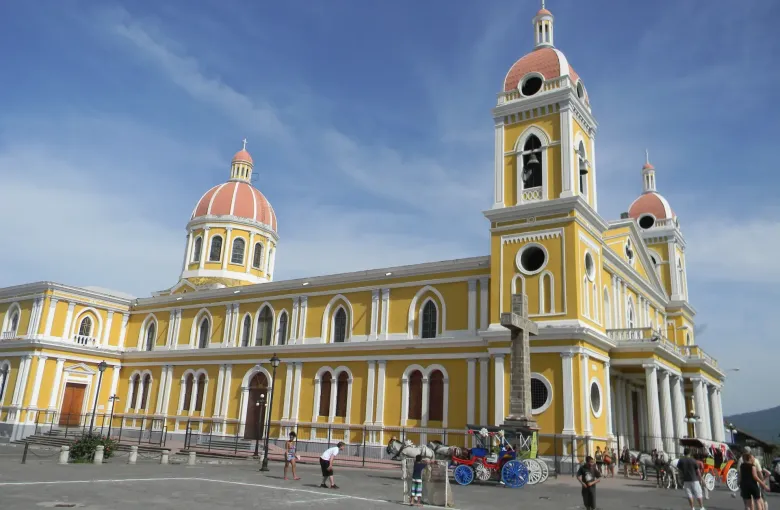 The yellow and terracotta towers of Granada Cathedral stand above horse carriages waiting on the plaza.