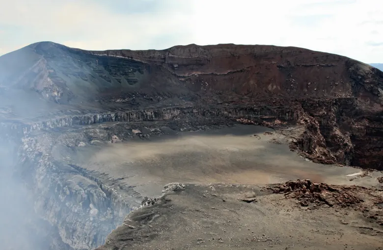 Gas drifts across the layered rock walls and gray ash floor of the caldera at Masaya volcano.