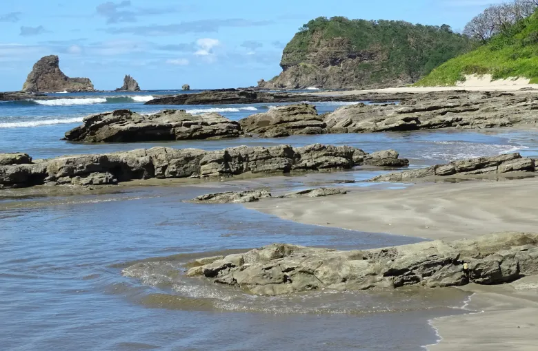 Low tide exposes flat rock shelves along a Pacific beach north of San Juan del Sur under a clear sky.
