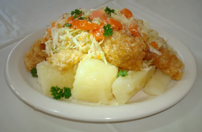 A plate of vigoron sets boiled yuca and fried pork rind under a topping of shredded cabbage and tomato.