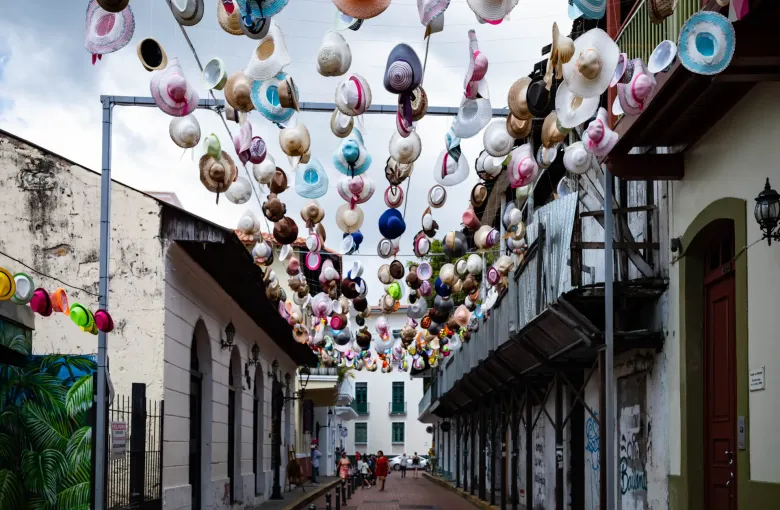 A narrow colonial street in Casco Viejo, Panama City, strung overhead with hundreds of colored hats.