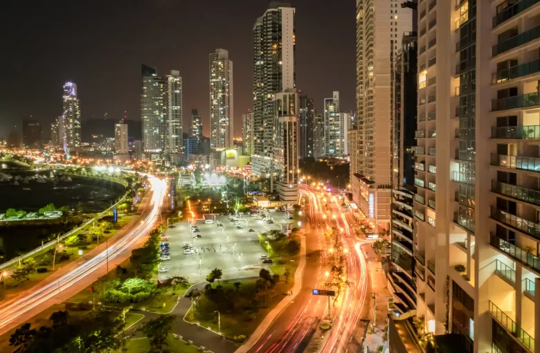 The Panama City skyline at night above the curve of the seafront road, with traffic trails below.