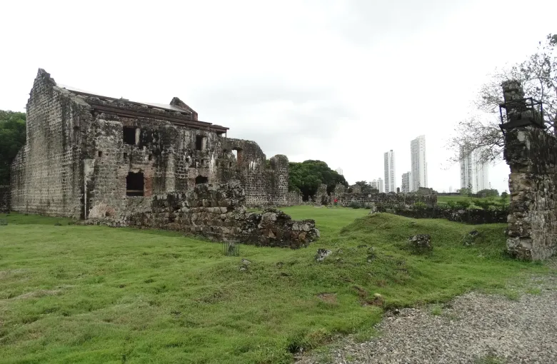 The roofless stone walls of a convent at Panama Viejo standing on flat grass, with the modern skyline behind.