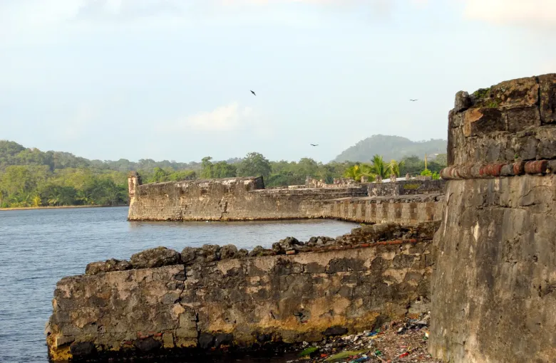 The weathered stone batteries of the Portobelo fortifications running along the bay, with green hills behind.