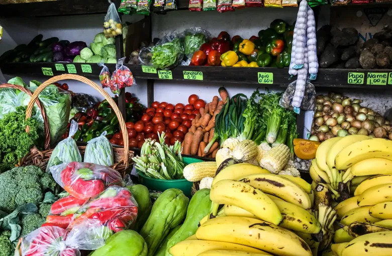A Panamanian produce stall stacked with bananas, chayote, tomatoes and greens under hanging goods.