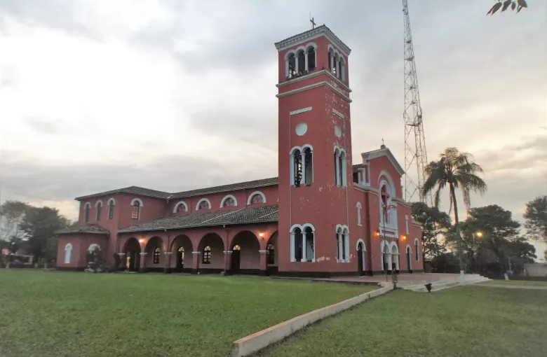 The rose colored parish church of San Jose at Ybycui stands behind its lawn and arcade at dusk.