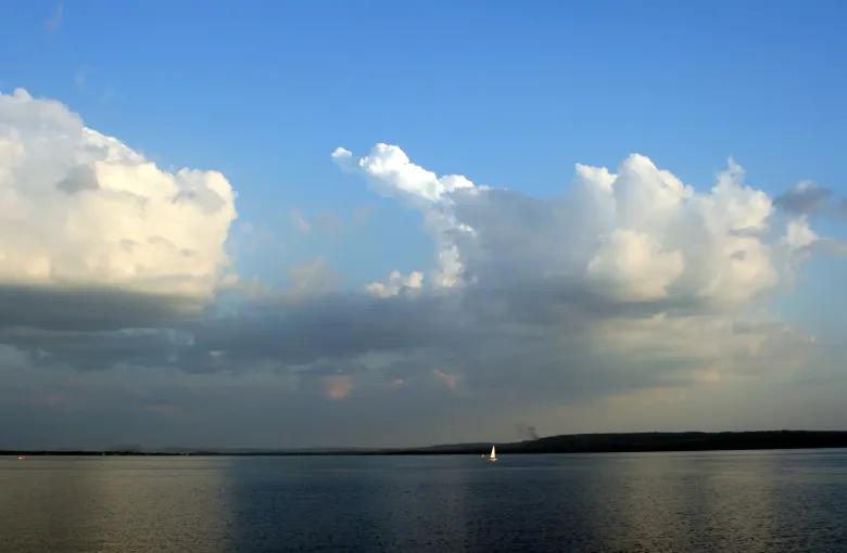 A single sailboat crosses the calm water of Lake Ypacarai under tall afternoon cloud.