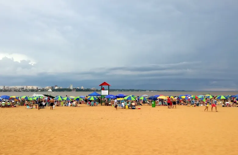 Ranks of colored parasols line the sand at Playa San Jose in Encarnacion as a storm front builds over the Parana.