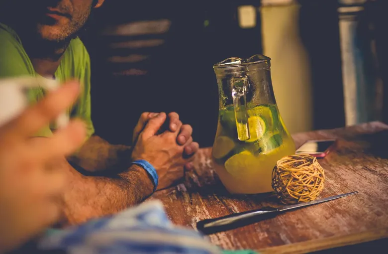 A guampa of terere packed with yerba and a metal bombilla is passed between two people at an outdoor table.