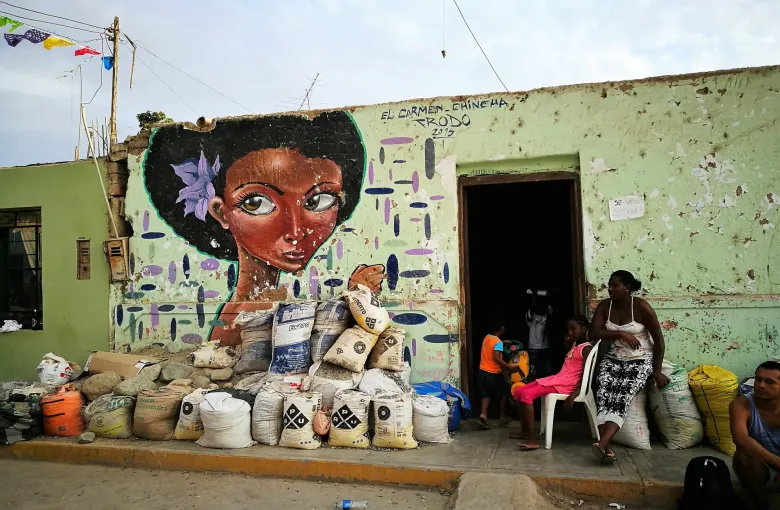 A painted mural of an Afro-Peruvian woman on a wall at El Carmen in Chincha, with sacks of produce stacked beneath it.