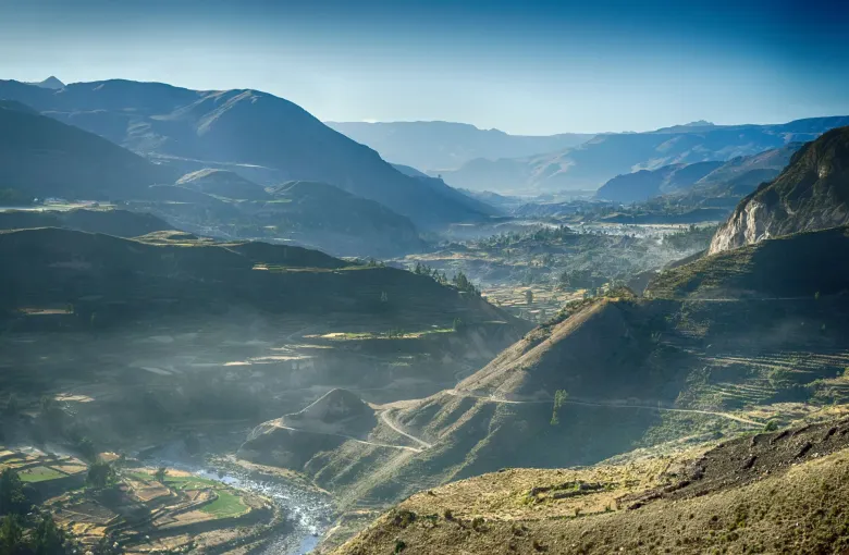 Terraced fields along the floor of the Colca Canyon in the Arequipa region with the river below and ridges in haze beyond.
