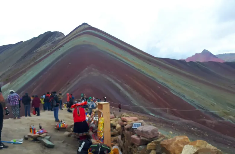 The banded red and ochre slopes of Vinicunca in the Cusco region with visitors standing on the ridge below the summit.