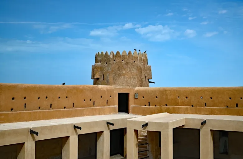 The restored mud brick fort at Al Zubarah, with a crenellated wall and corner tower against a clear sky