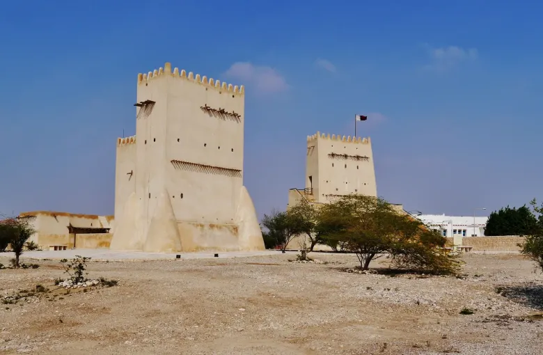 Two pale watchtowers with crenellated tops standing above a low stone wall at Umm Salal Mohammed