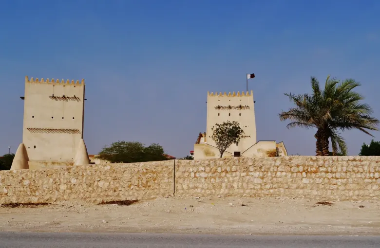 The two Barzan watchtowers seen across scrub and low walls under a deep blue sky