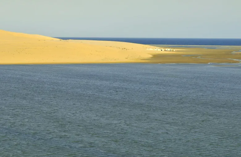 A long dune ridge meeting the still water of the inland sea in southern Qatar