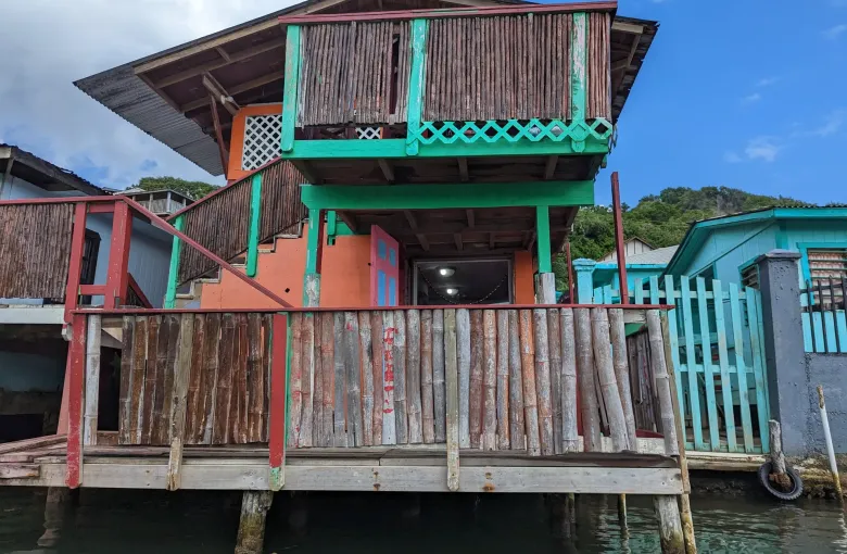 A timber house on stilts over the water, painted in turquoise, red and blue.