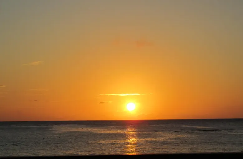 The sun low on a clear horizon over calm sea, seen from the shore of Roatan.