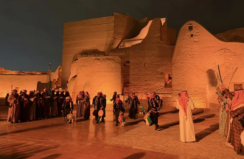 Performers in traditional dress lined up for the Najdi ardha sword dance against the floodlit mud-brick walls of At-Turaif in Diriyah, Saudi Arabia.