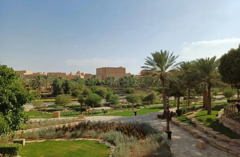 The mud-brick walls of the At-Turaif district at ad-Dir'iyah, Saudi Arabia, rising beyond the palms and lawns of the Wadi Hanifah gardens.