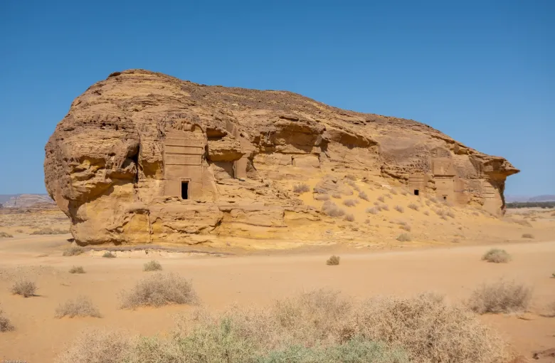 A Nabataean tomb carved into a sandstone outcrop at Hegra near AlUla, Saudi Arabia, its doorway and facade cut from the living rock.