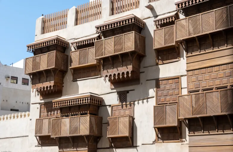 Carved wooden rawashin balconies stacked across the coral-stone facade of a merchant house in Historic Jeddah, Saudi Arabia.